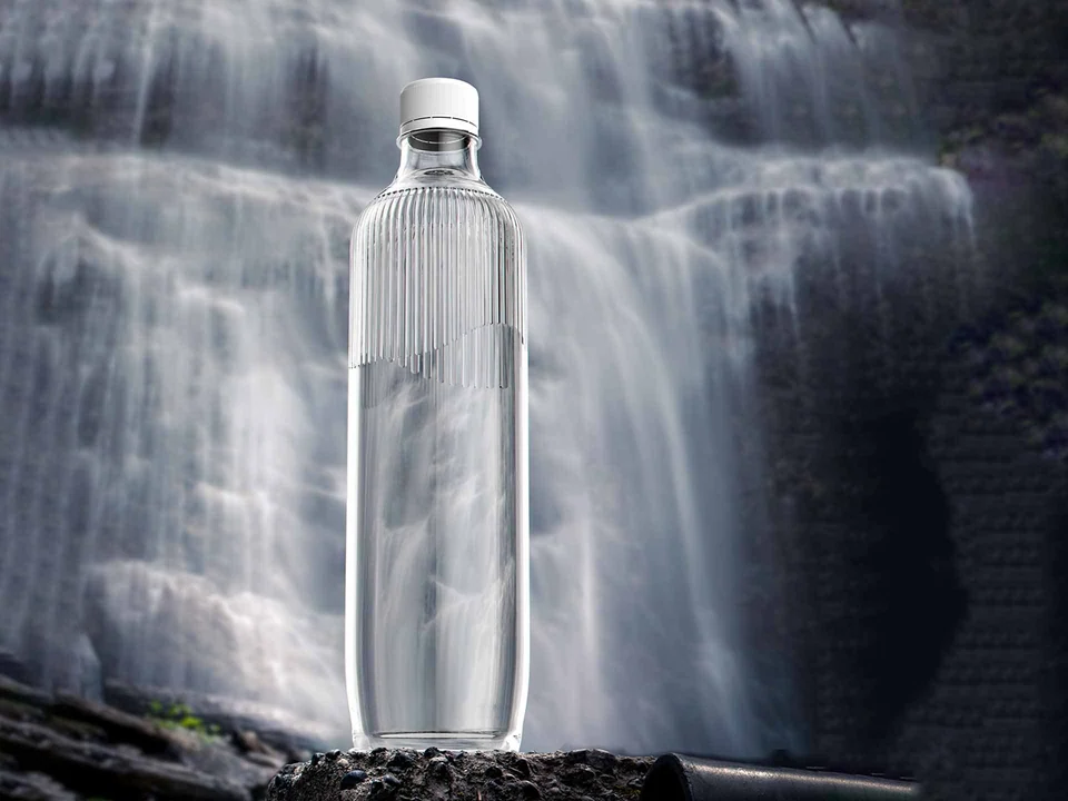 Transparent ribbed bottle standing in front of a waterfall